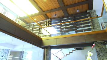 Un vaste espace de vie doté d’un haut plafond, de poutres en bois, d’un escalier et de meubles en osier.