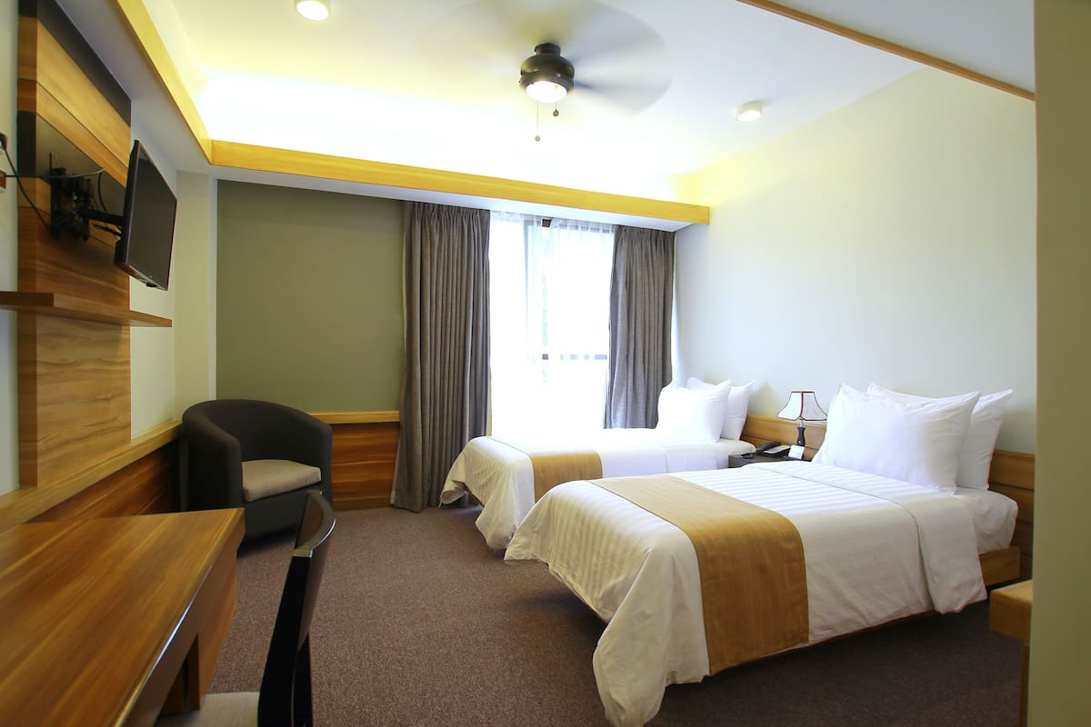 Ein Hotelzimmer mit zwei Betten, einem Schreibtisch, einem Sessel, einem Fernseher und einem Deckenventilator.
