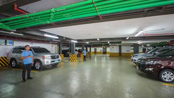 A multi-level parking garage with cars parked on different levels, green pipes on the ceiling, and yellow and black striped barriers.