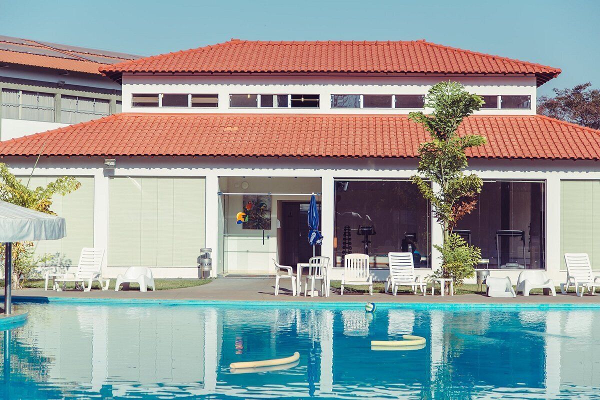 Un bâtiment à deux étages, doté d’un toit recouvert de tuiles rouges, d’une piscine avec des chaises longues et d’un patio couvert.