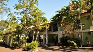 A building with a two-story structure, surrounded by palm trees and other tropical vegetation. - Hotel Água das Araras (Paraguacu Paulista)