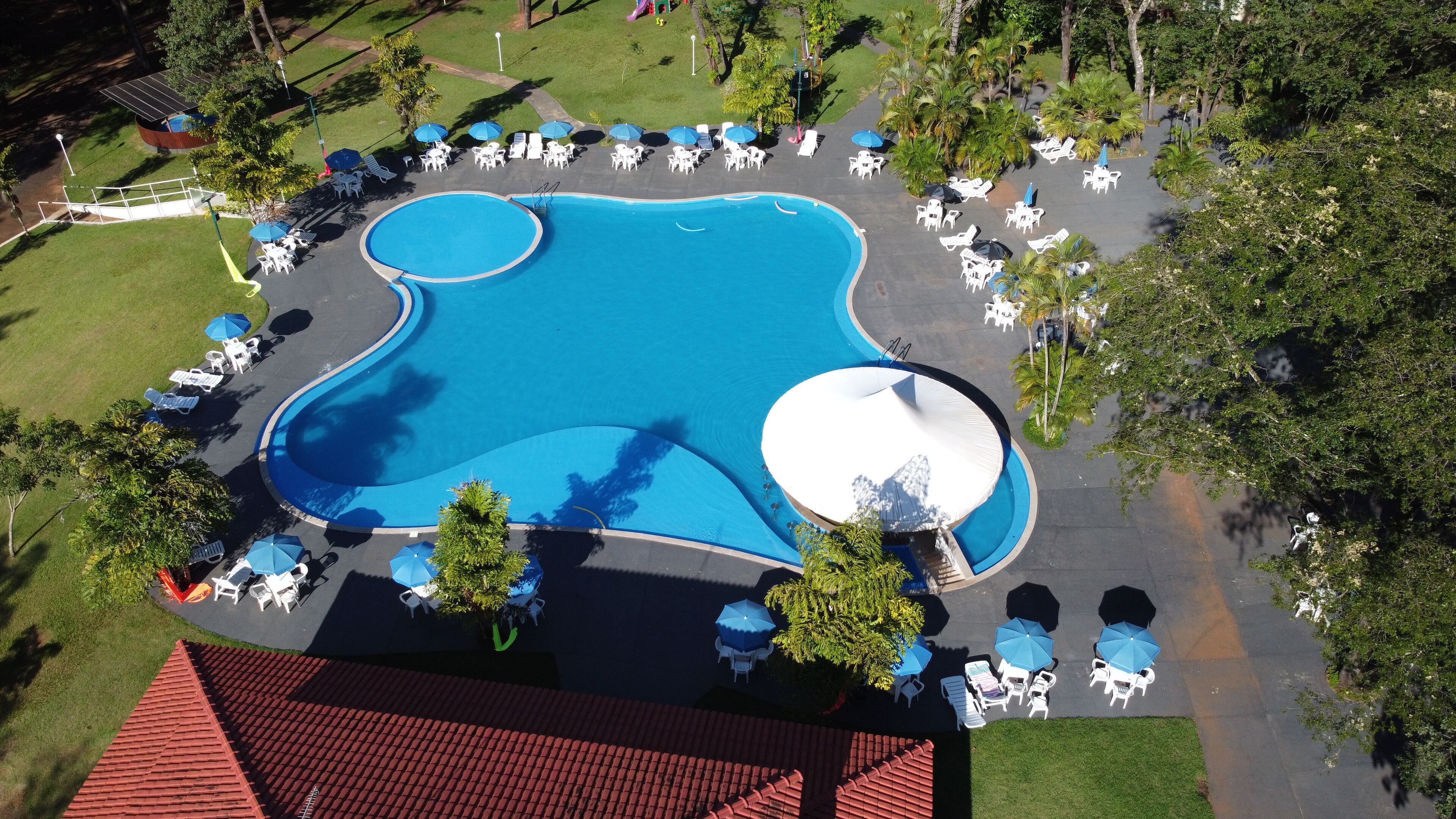 An aerial view of a resort with a large swimming pool, sun loungers, and umbrellas.