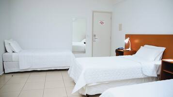 Habitación de hotel con dos camas individuales, cabecera de madera, mesita de noche con lámpara y una puerta con un cartel.