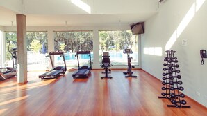 A spacious gym with exercise equipment, large windows, and a view of a pool. - Hotel Água das Araras (Paraguacu Paulista)