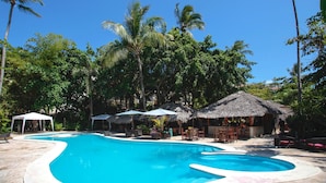 A swimming pool with lounge chairs and umbrellas, surrounded by palm trees and thatched-roof structures. - Corales Colonial II With Private Beach,los Corales (Punta Cana)