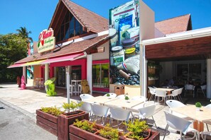 A gift shop with a sign, outdoor seating area with tables and chairs, and potted plants.