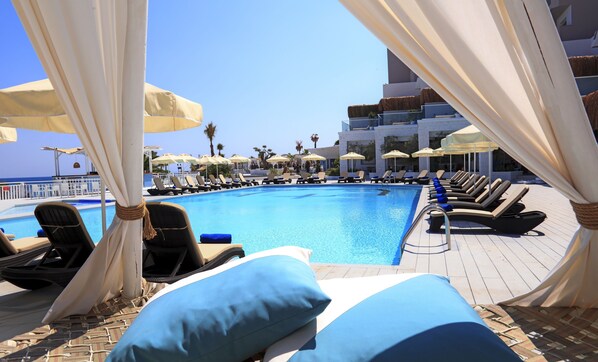A pool area with lounge chairs and umbrellas, a clear blue sky, and a view of the sea. - Design Plus Seya Beach Hotel (Cesme)