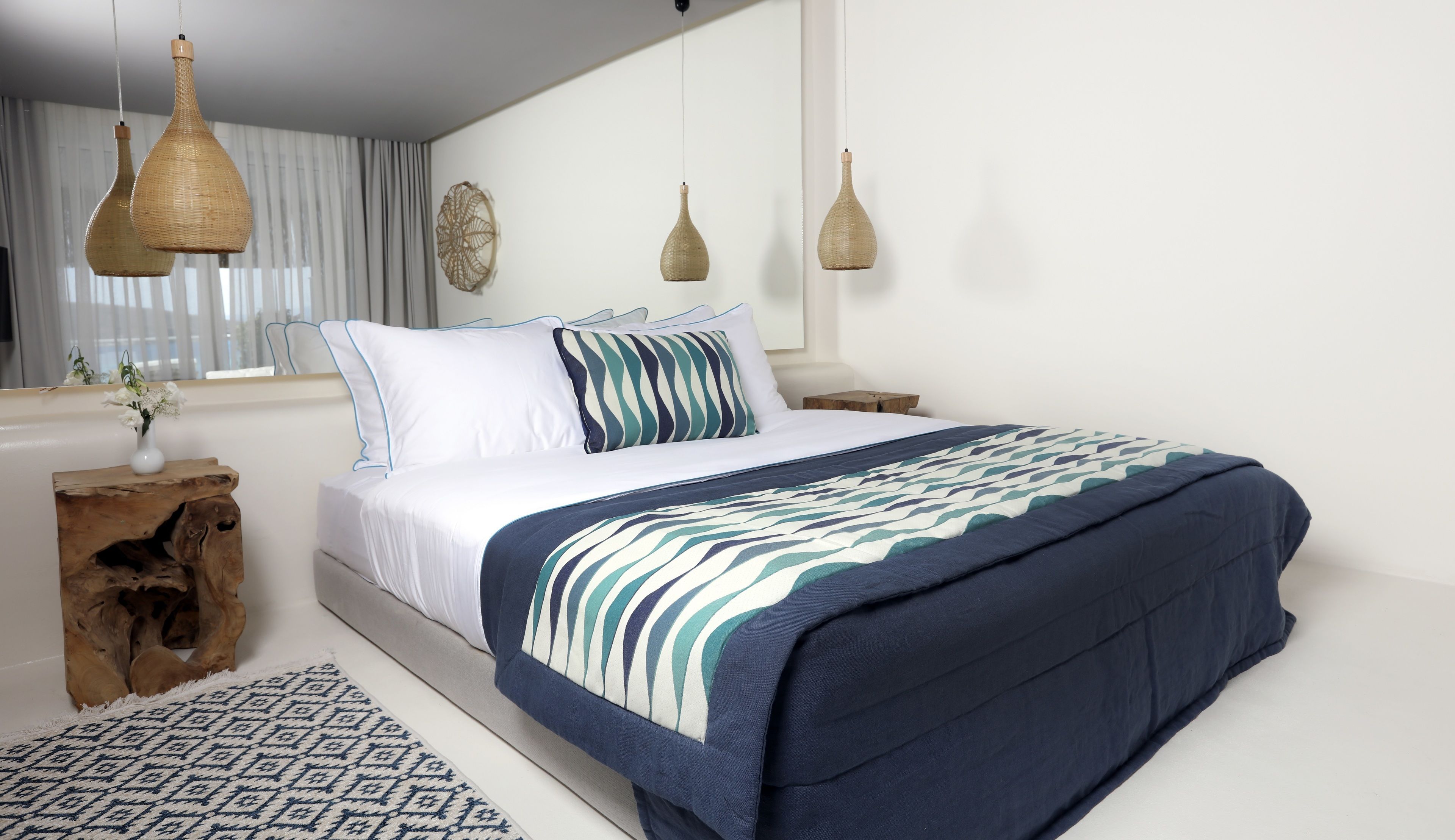 A neatly arranged bedroom with a bed, bedside tables, a decorative wall piece, and hanging lamps.