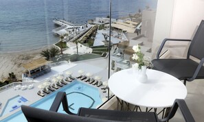 A balcony with a view of a pool, lounge chairs, and a dining table with a vase of flowers. - Design Plus Seya Beach Hotel (Cesme)