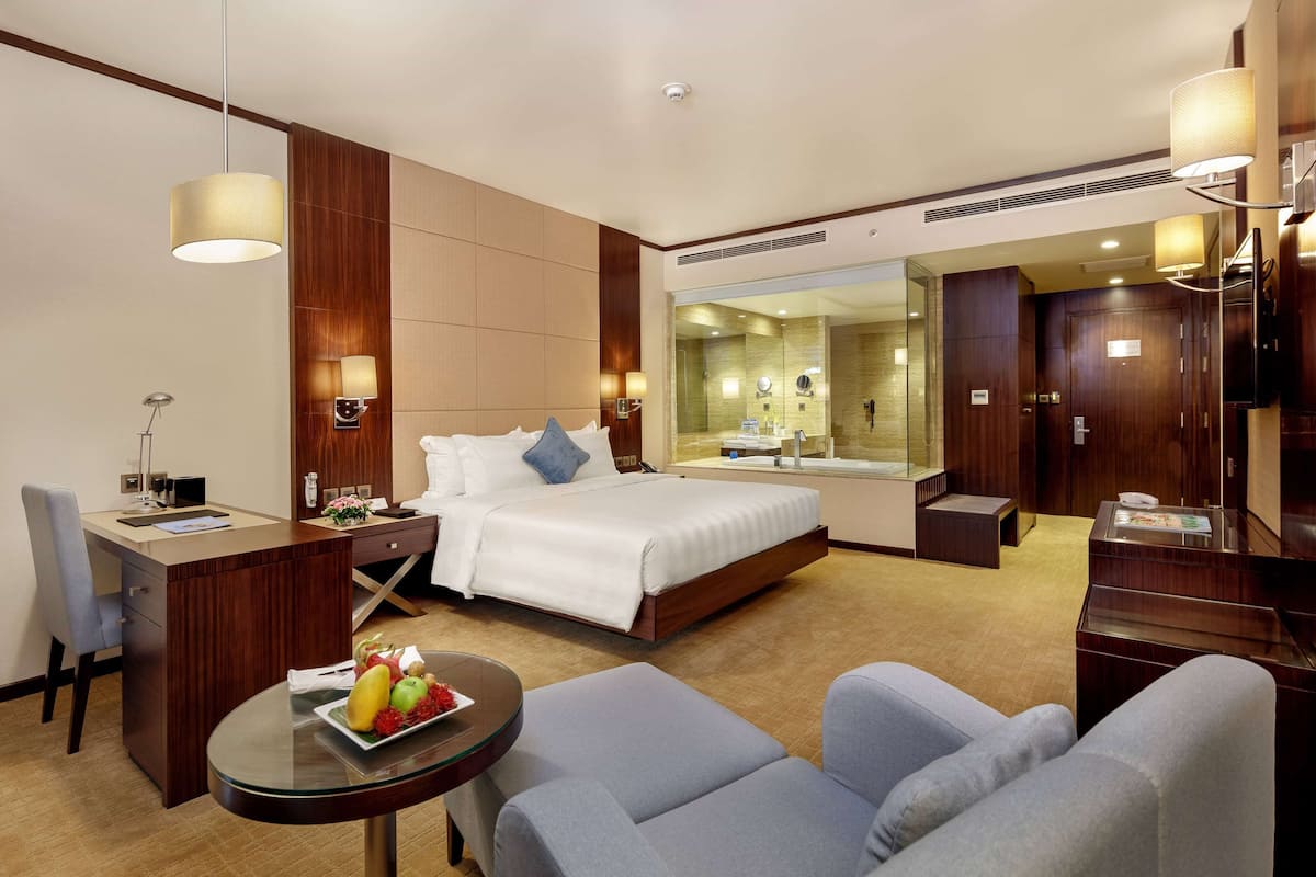 A hotel room with a bed, desk, chair, and a small table with fruit.