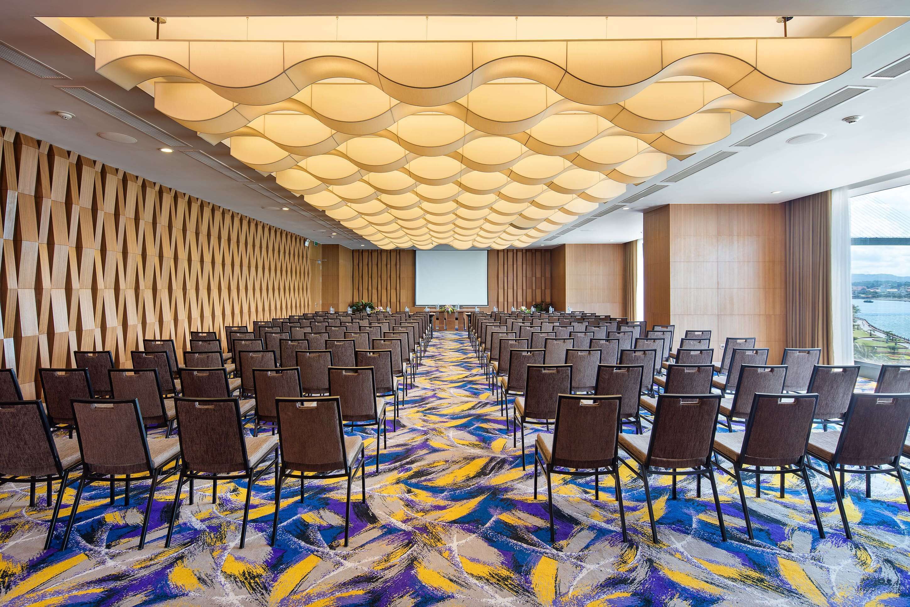 A conference room with rows of chairs, a patterned carpet, and a modern ceiling design.