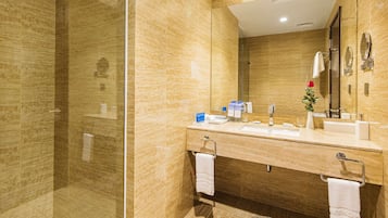 Un baño moderno con ducha de vidrio, un espejo grande y tocador con lavamanos y toalleros.