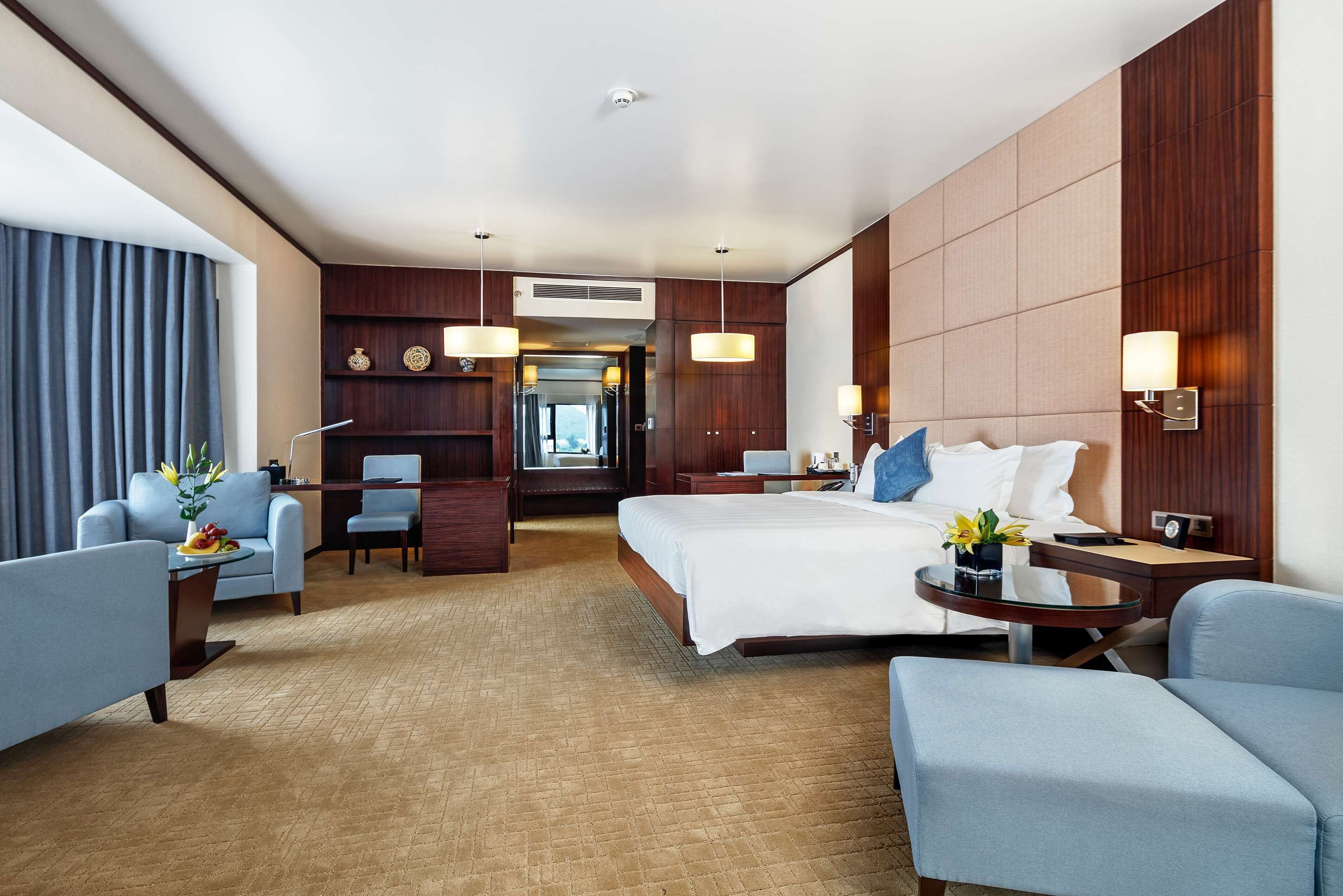 A hotel room with a large bed, two armchairs, a desk, and a dining area.