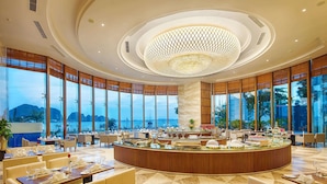 A spacious hotel lobby with a central bar, large windows offering a view of the sea, and a modern chandelier. - Wyndham Legend Halong Hotel (Bai Chay)