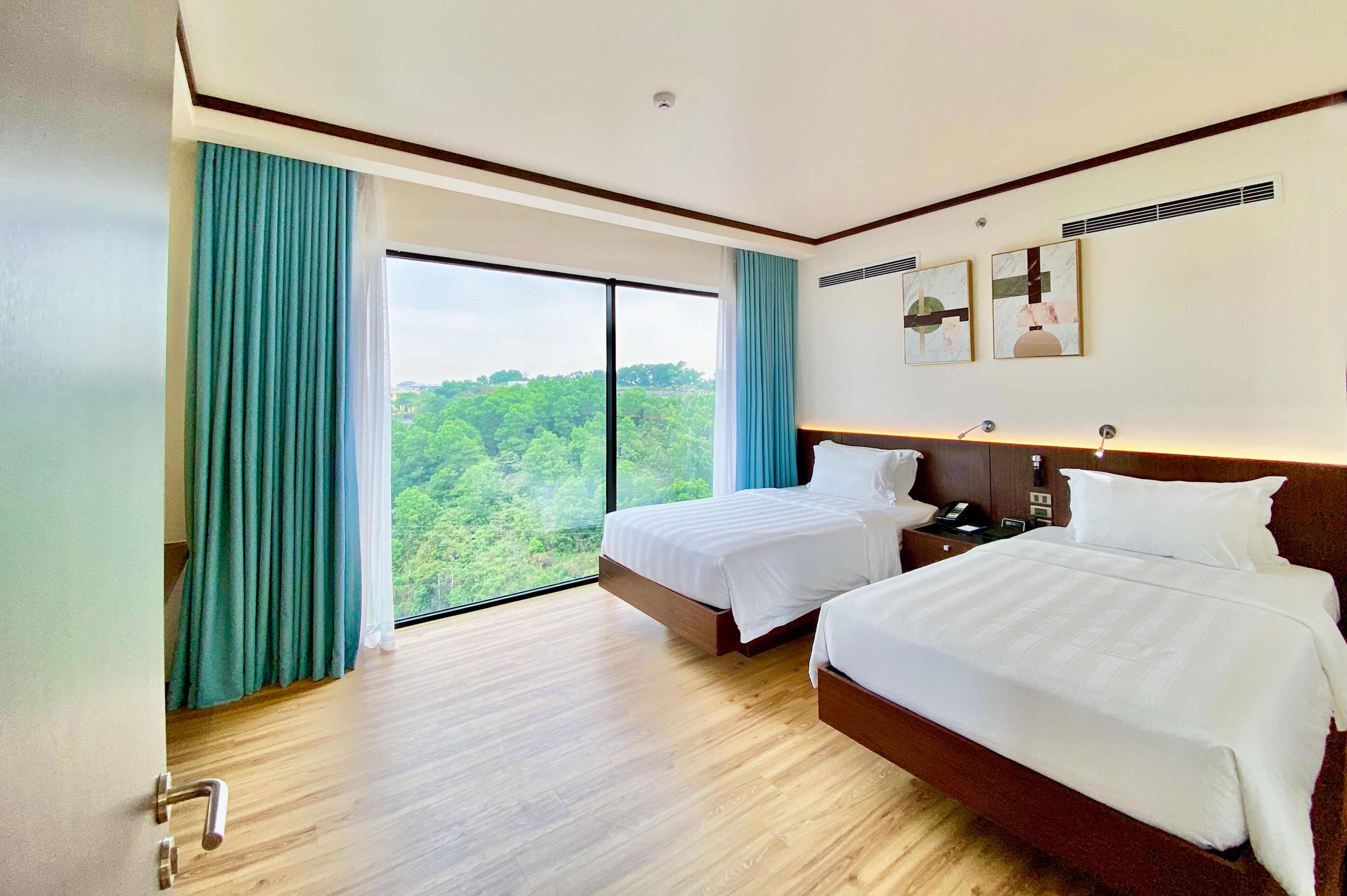 Habitación de hotel con dos camas, un ventanal con cortinas, suelo de madera y una obra de arte en la pared.