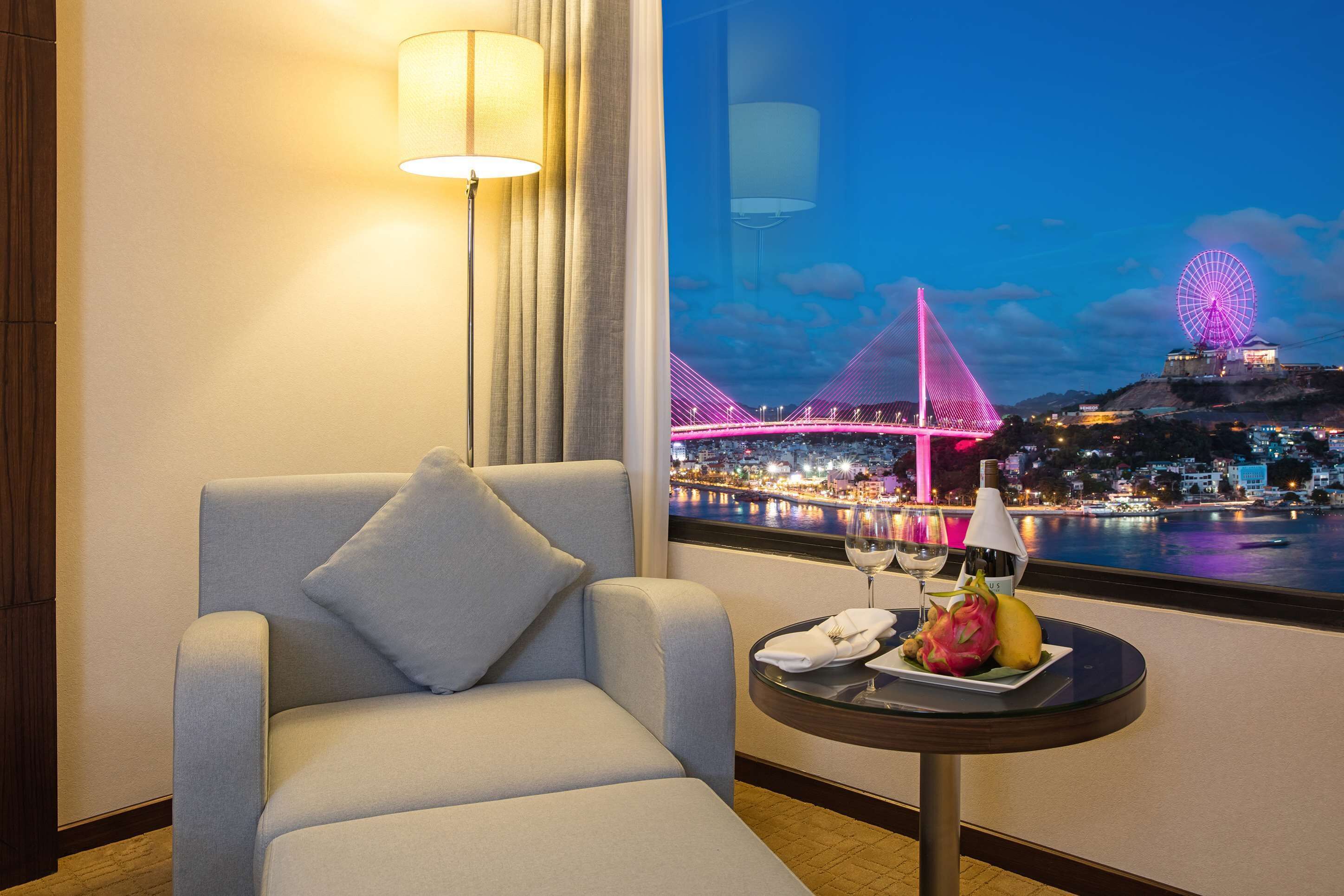 Une chambre d’hôtel avec vue sur un pont illuminé et sur le paysage urbain nocturne.