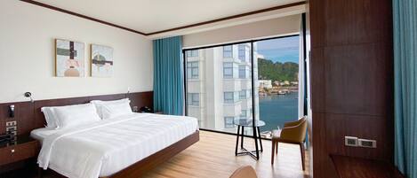 A hotel room with a large bed, a desk, a chair, and a view of a body of water and buildings.