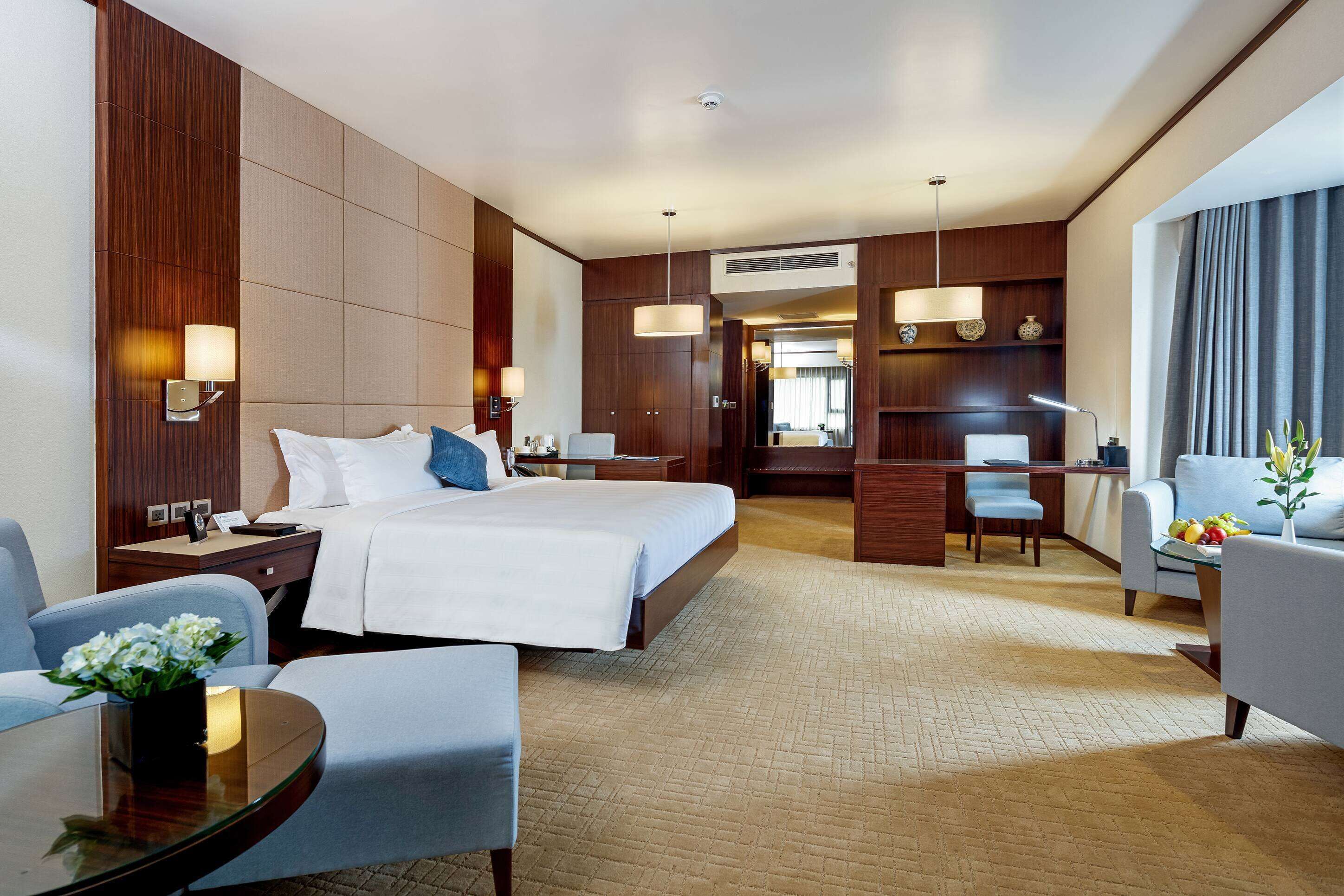 A hotel room with a large bed, a desk, a chair, a small table, and a sofa.