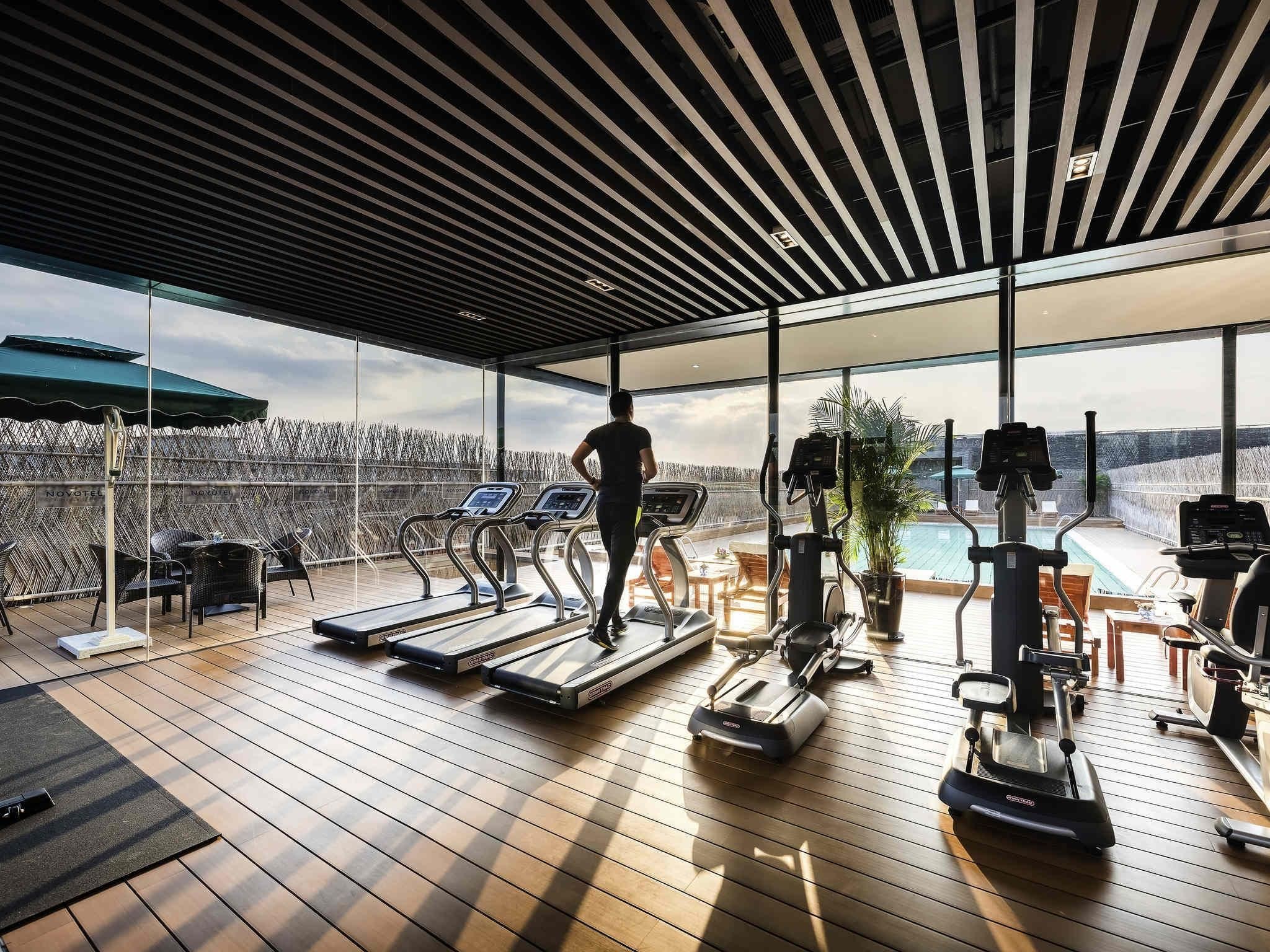A modern gym with treadmills, elliptical machines, and a pool view.