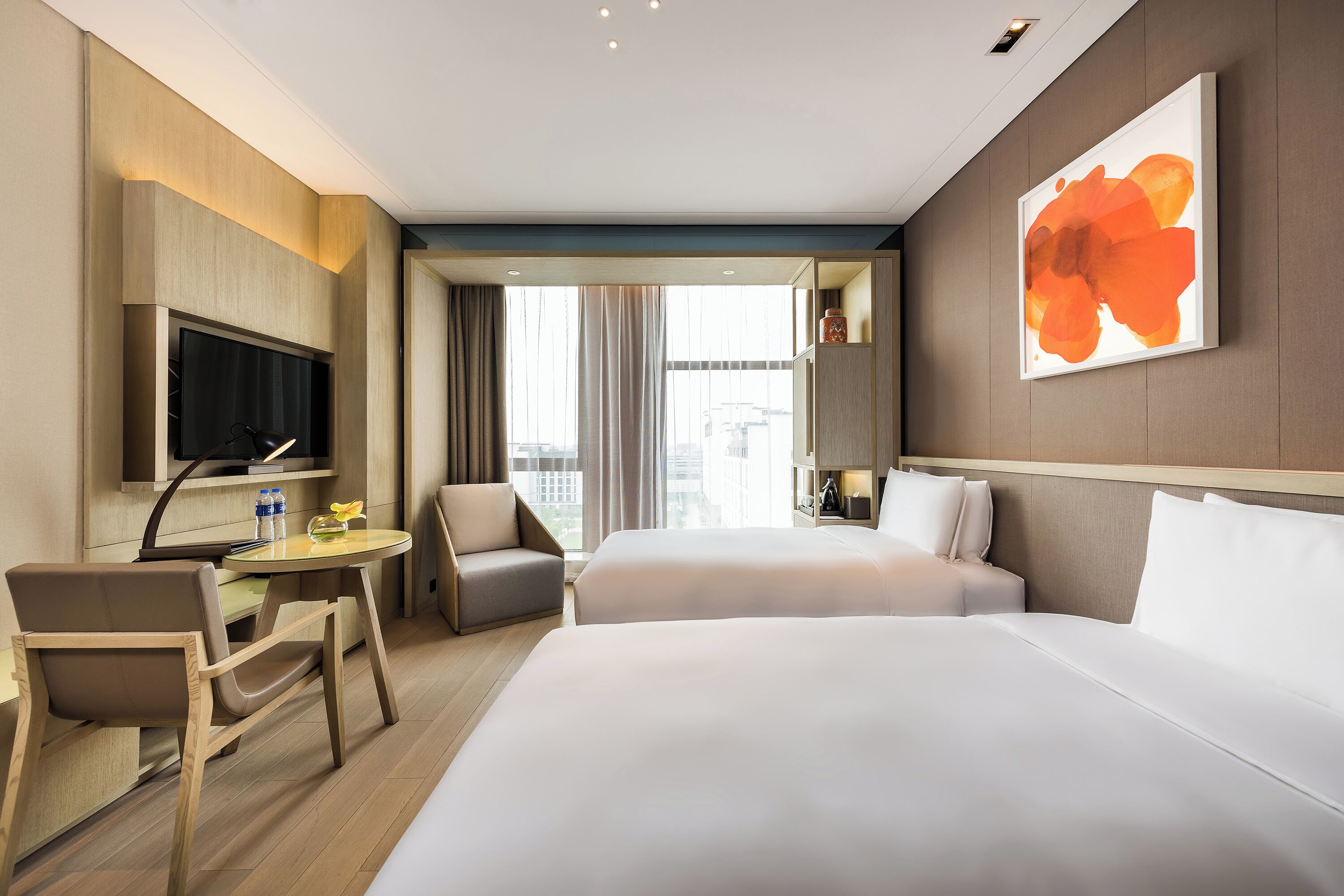 A hotel room with two beds, a desk, a chair, a TV, and a large window with curtains.