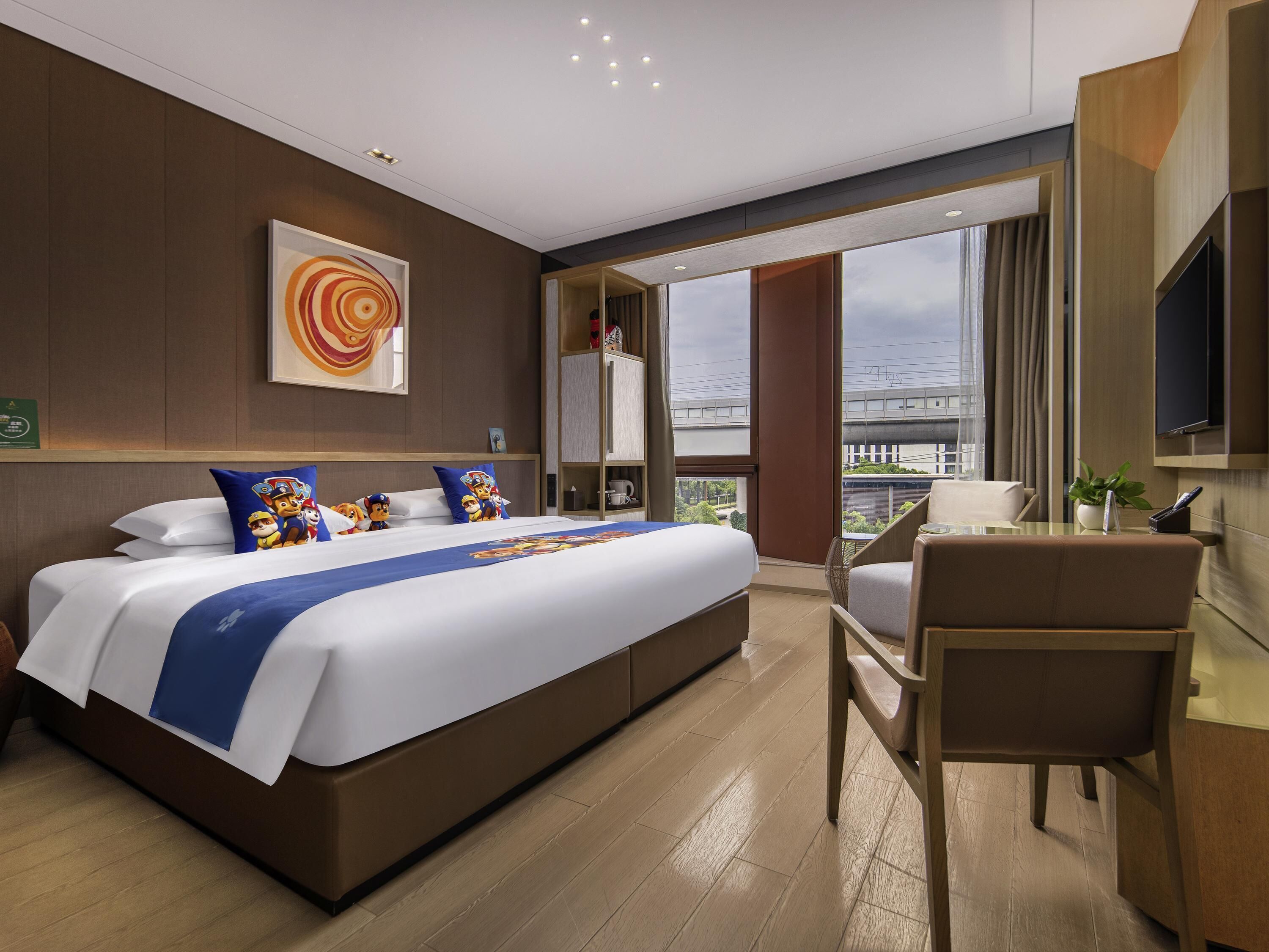 A modern hotel room with a large bed, a desk, and a view of the city.