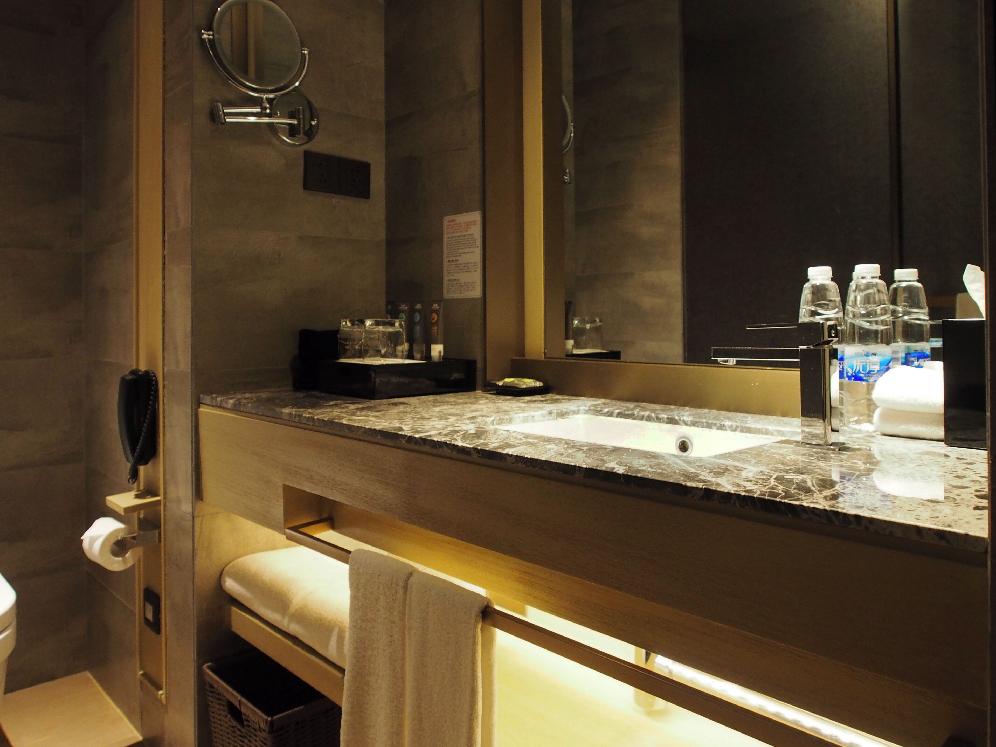A bathroom with a marble sink, a mirror, a towel rack, a toilet, and a trash bin.