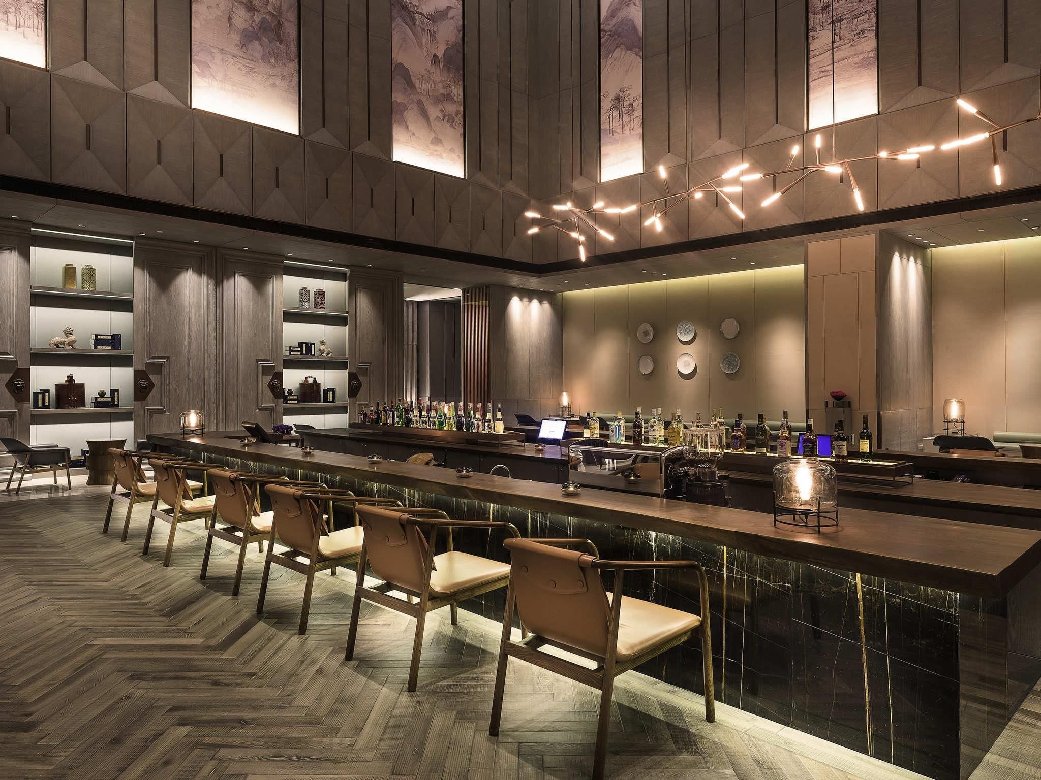 A modern bar area with a long counter, multiple seating options, and a variety of bottles and glasses.