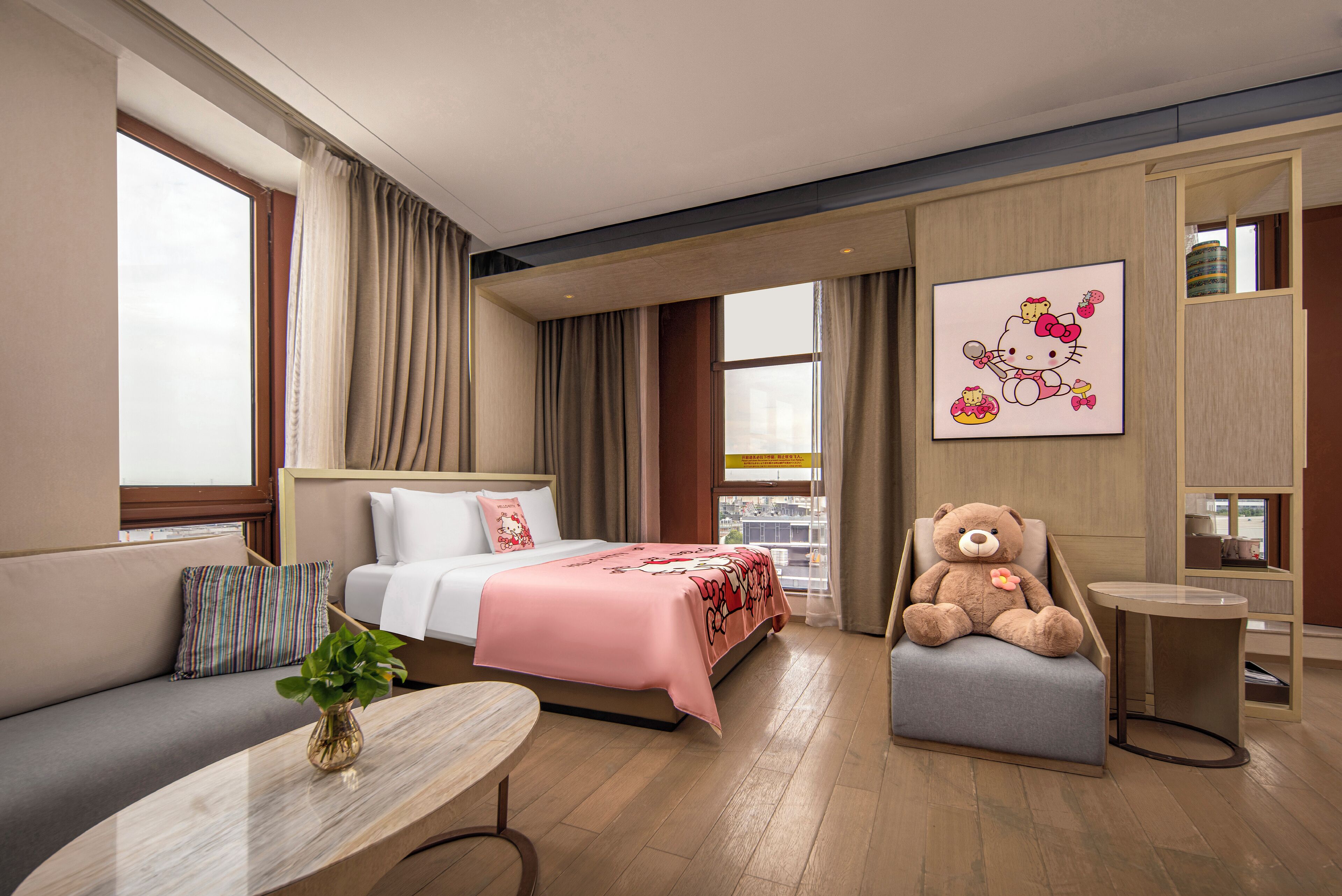 Quarto de hotel com cama, sofá, poltrona, mesinha e um urso de pelúcia grande.