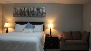 Une chambre à coucher avec un lit, deux tables de chevet avec des lampes, un canapé et un tableau représentant un paysage urbain accroché au mur.