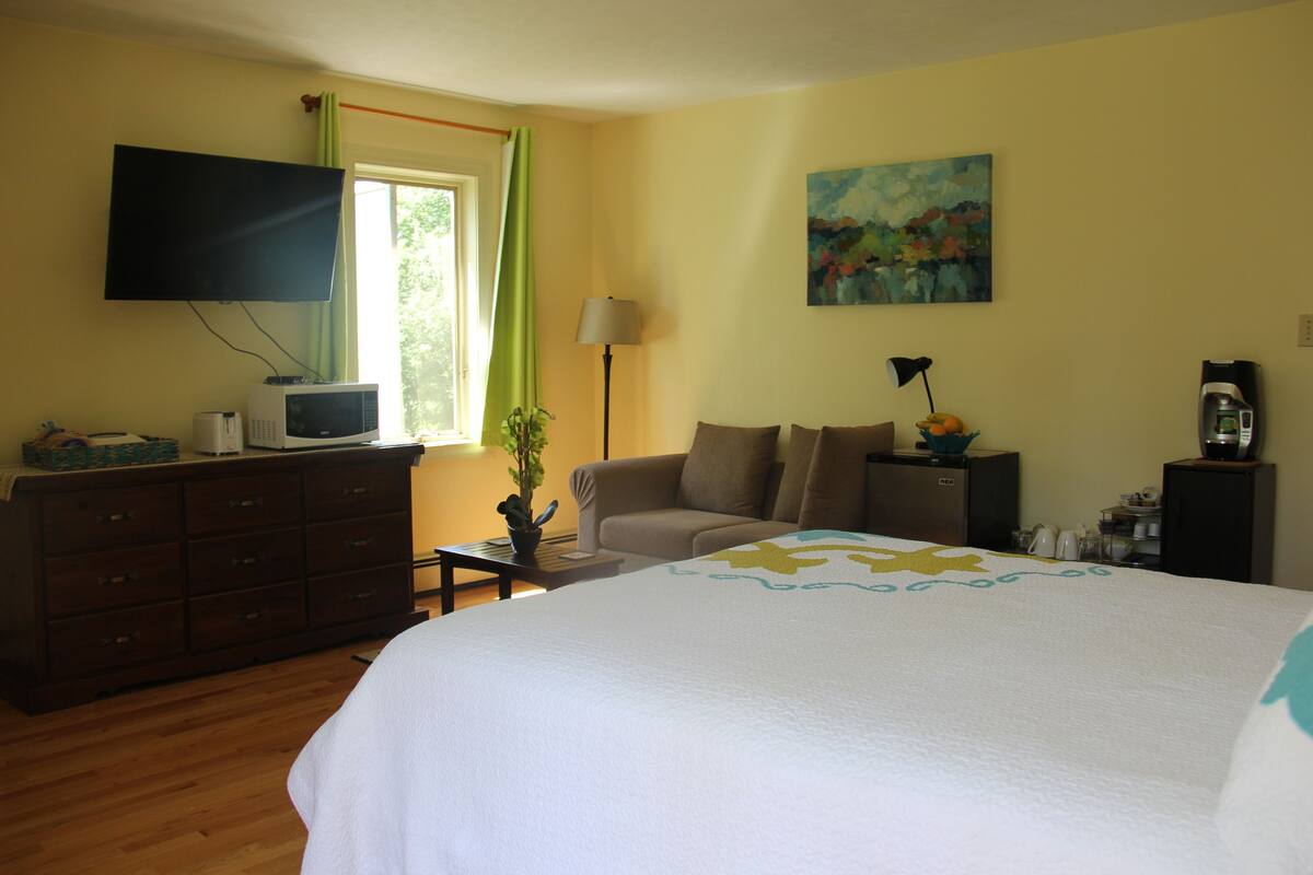 A hotel room with a bed, a television, a desk, a lamp, a coffee maker, and a painting on the wall.