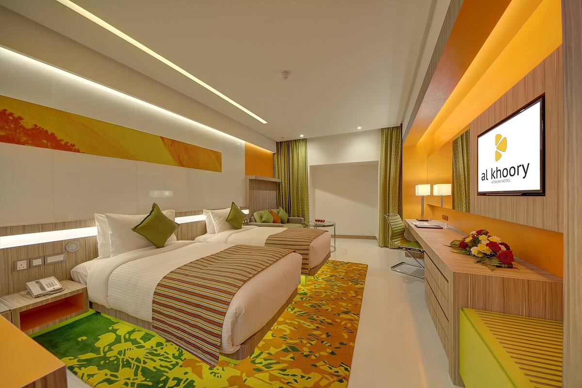 A modern hotel room with two beds, a desk, and a reception area.
