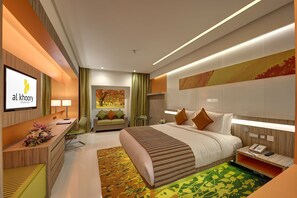 Een moderne hotelkamer met een groot bed, een bureau met een computer, een televisie en een receptiebalie.