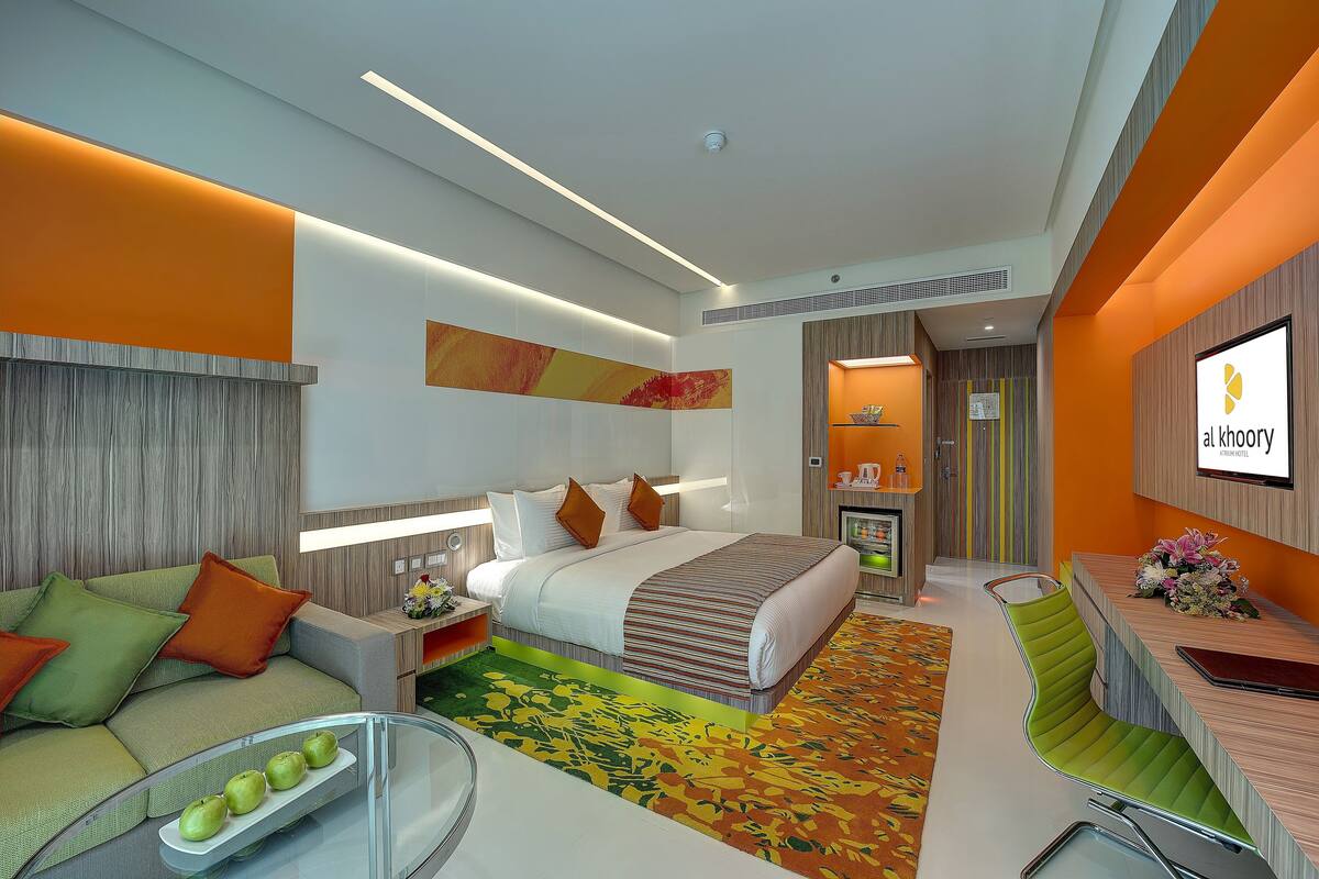 A modern hotel room with a bed, a sofa, a desk, and a bathroom.