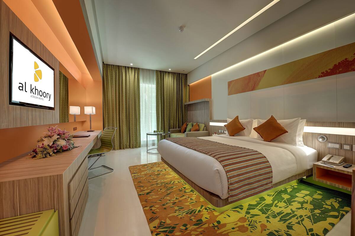 A modern hotel room with a large bed, a desk with a computer, a TV, and a desk lamp.