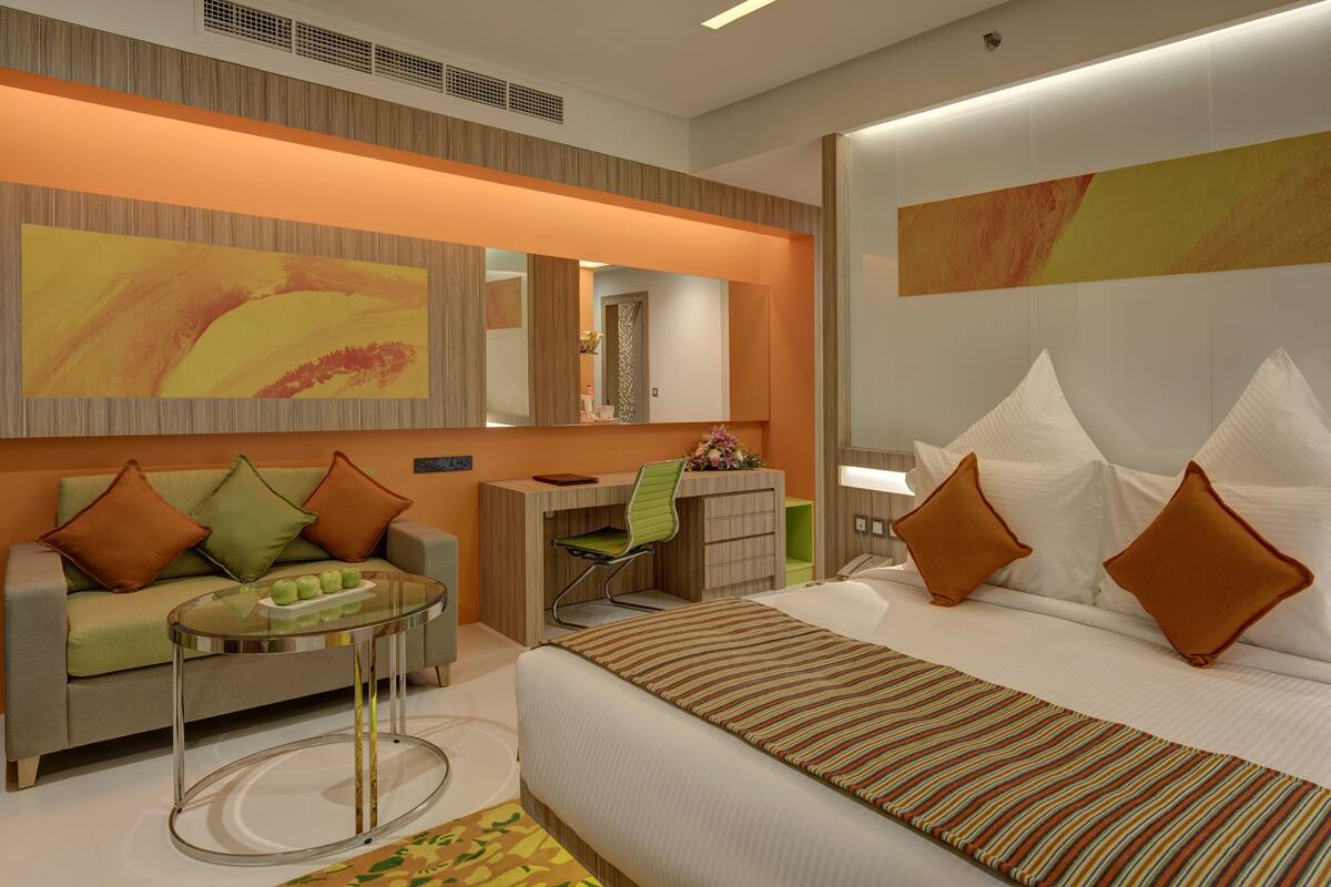 A modern hotel room with a bed, a desk, a sofa, and a glass coffee table.