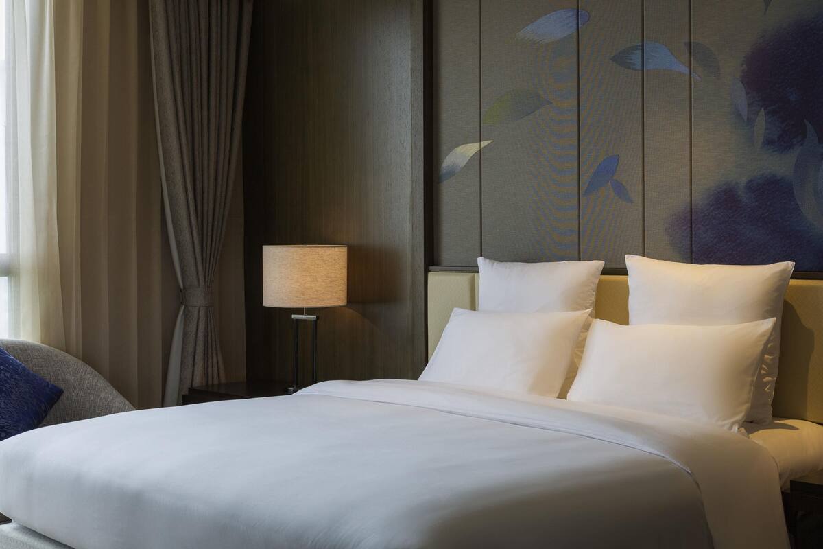 Quarto de hotel com uma cama grande, mesa de cabeceira com abajur e parede com padrão de pássaros.