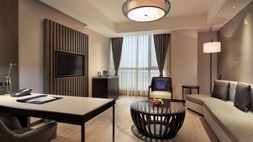 A modern hotel room with a TV, a round coffee table, a sofa, and a dining table.