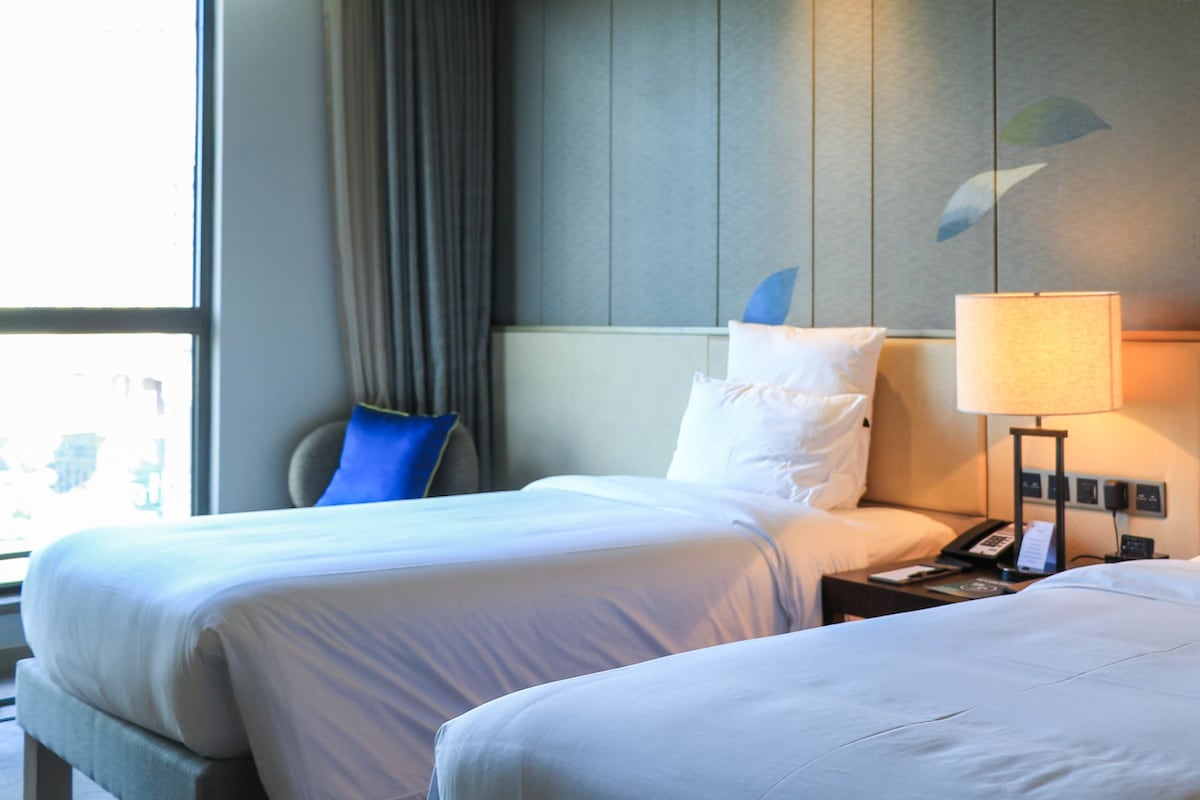 Una habitación de hotel con dos camas, una mesita de noche con lámpara y una ventana con cortinas.