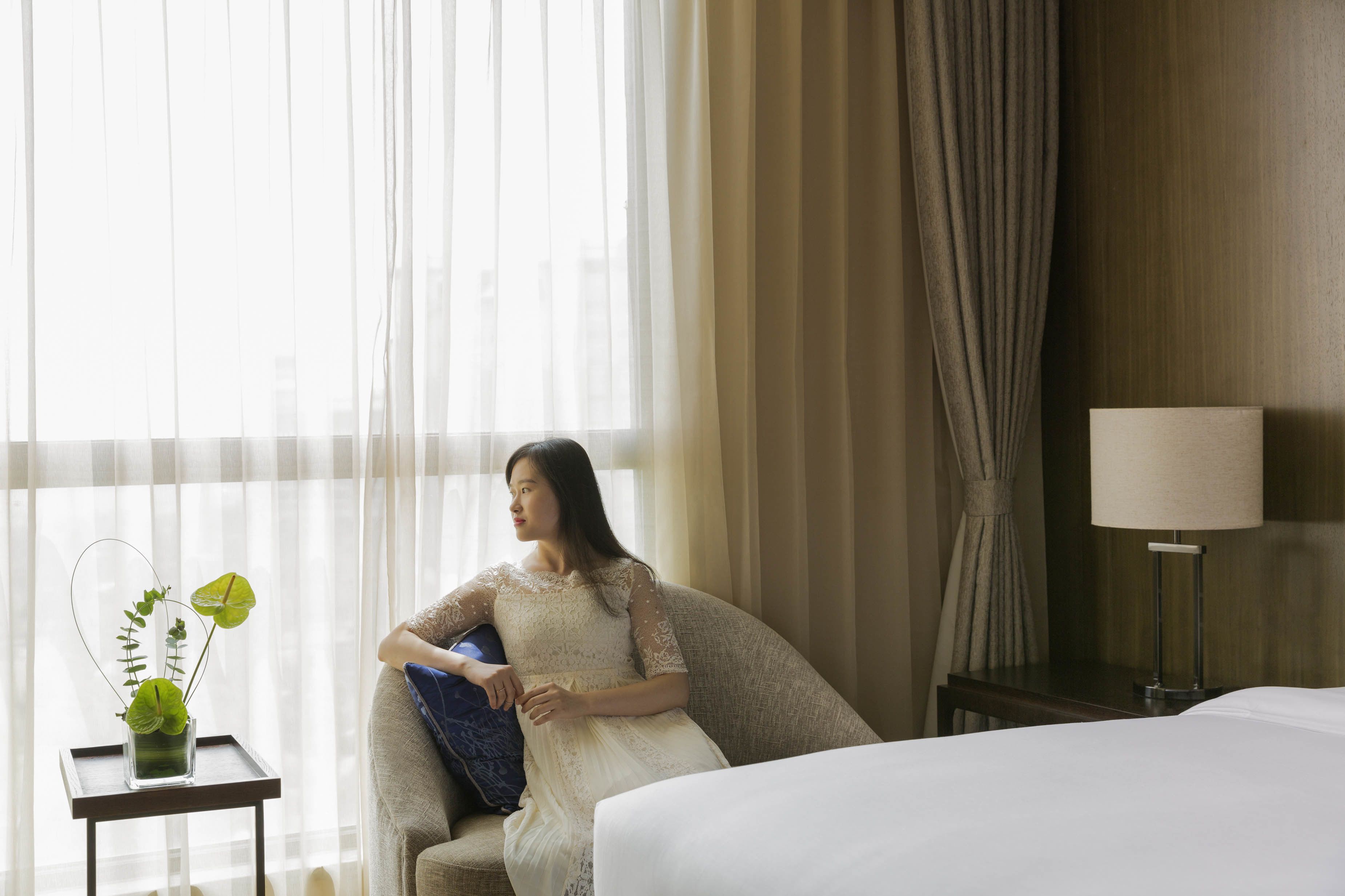 Une chambre d’hôtel avec un lit, une chaise, une lampe et une plante posée sur une table d’appoint.
