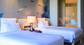 Una habitación de hotel con dos camas, una mesita de noche con lámpara y una pared con un mural de peces.