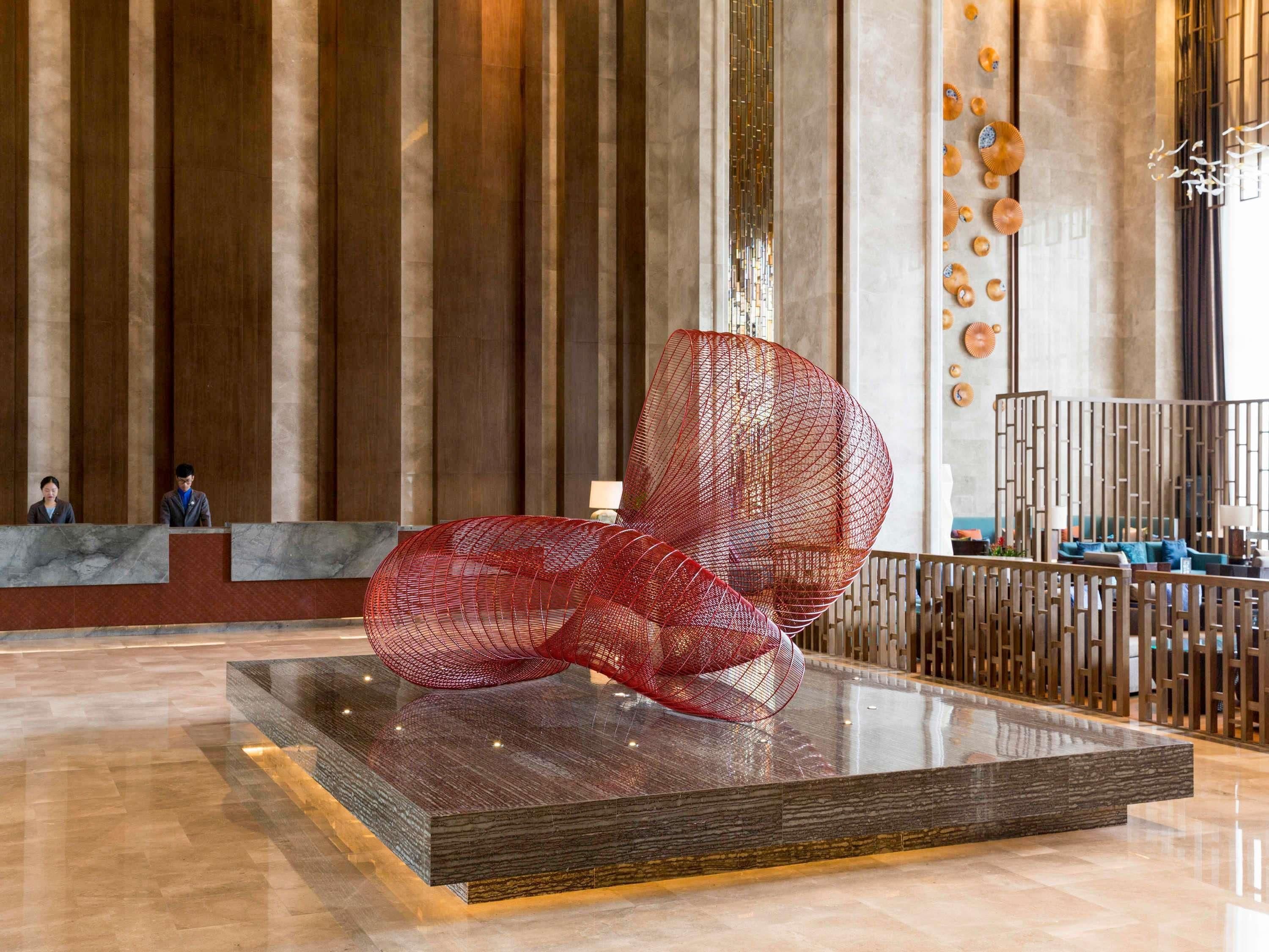 Un hall d’entrée moderne agrémenté d’une grande sculpture abstraite rouge, d’un comptoir d’accueil en marbre et d’une cloison en bois avec un canapé.