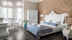 Ein Schlafzimmer mit Backsteinwand, einem weißen Bett, einer Kristallleuchtre und einem Essbereich mit Stühlen und Tisch.