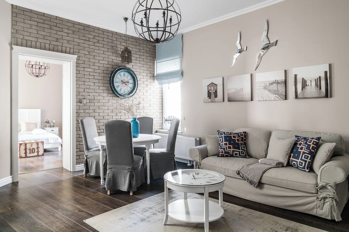 A living room with a brick wall, a round coffee table, a sofa with patterned cushions, and a dining area with chairs and a table.