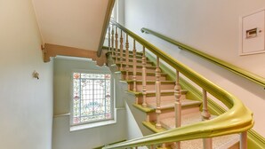 Eine Treppe mit hölzernen Spindeln und einem grünen Geländer, die zu einem Raum mit einem Fenster führt, dessen floralem Glasdekor.