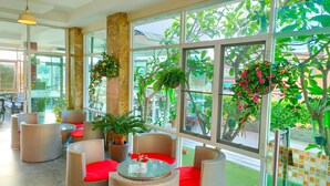 Un amplio espacio interior con mobiliario de mimbre, ventanas grandes y plantas en macetas.