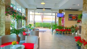 Un vestíbulo de hotel con mobiliario de mimbre, cojines rojos y plantas en macetas.