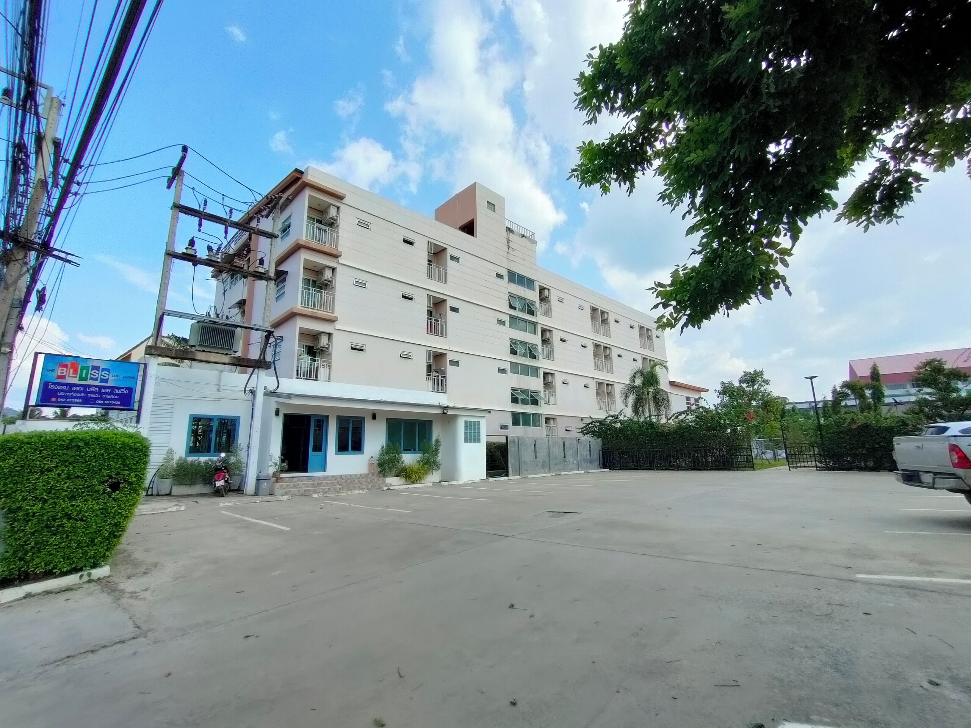 A multi-story building with a flat facade, balconies, and a parking area in front.