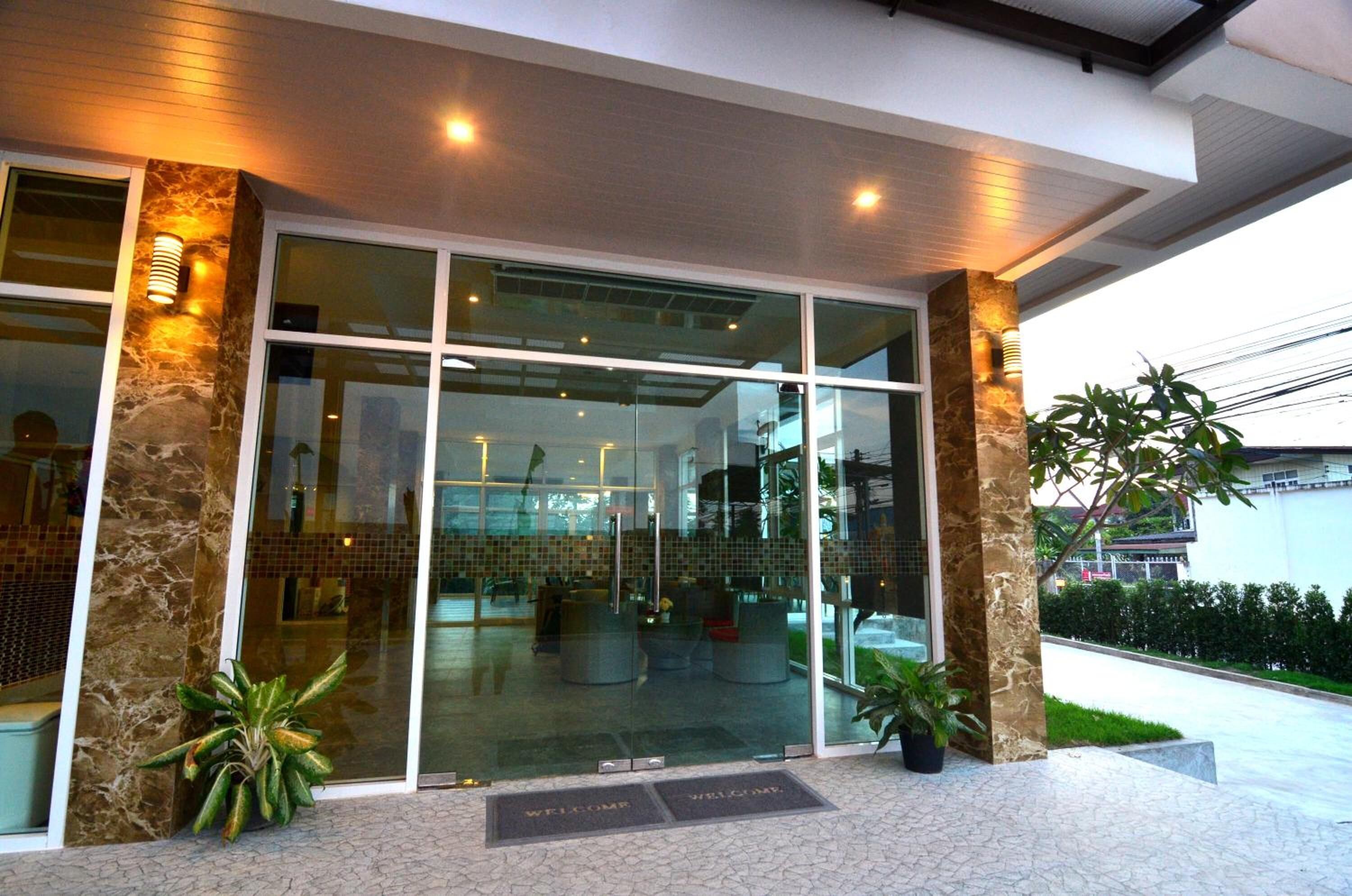 Una entrada moderna de edificio con puertas de vidrio, pilares de piedra y plantas en macetas.