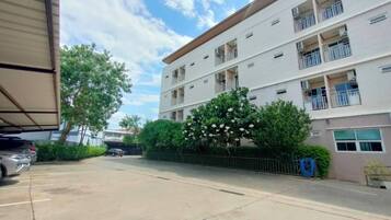 Un edificio de varios pisos con balcones, un estacionamiento y un árbol con flores blancas.