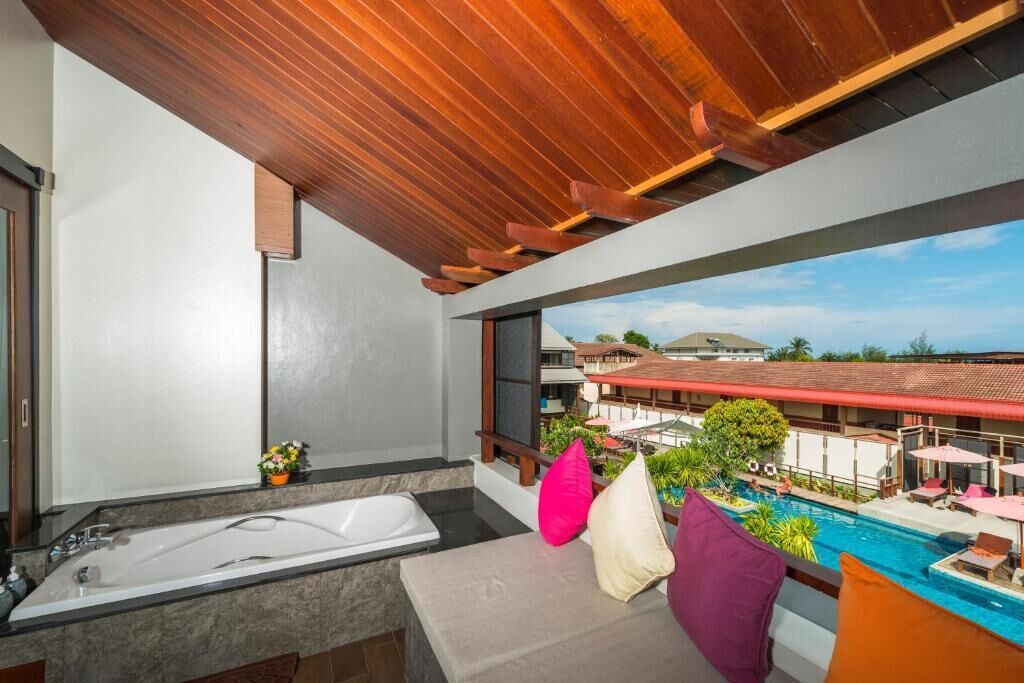 Un baño moderno con una bañera grande, un lavamanos pequeño y vistas a una piscina y edificios de un complejo turístico.